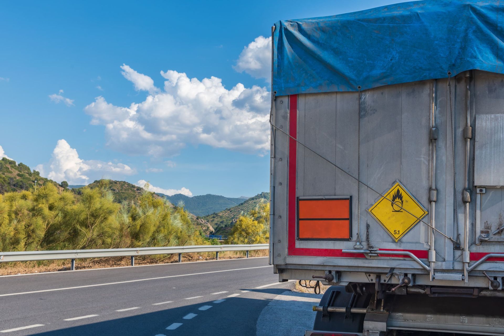 Un camión con una lona en la parte trasera circula por una autopista.