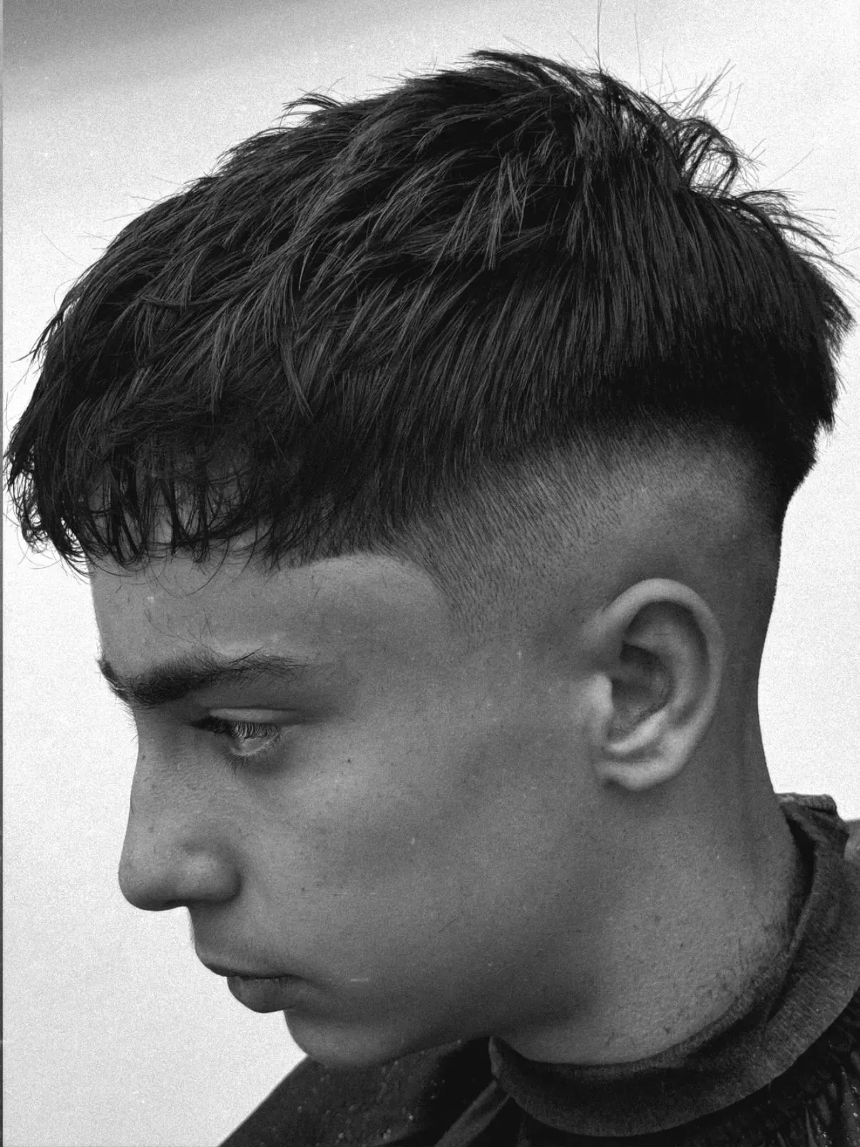 Persona con un corte de pelo oscuro y texturizado que presenta un desvanecimiento alto de la piel y mira hacia abajo.