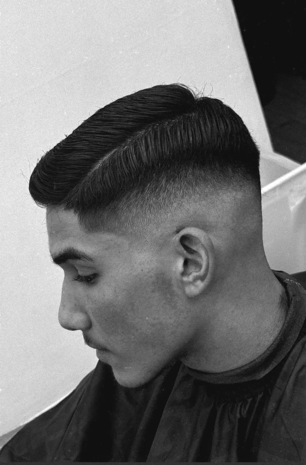 Hombre con corte de pelo alto degradado; cabello oscuro en la parte superior, que se desvanece hacia la piel en los lados.
