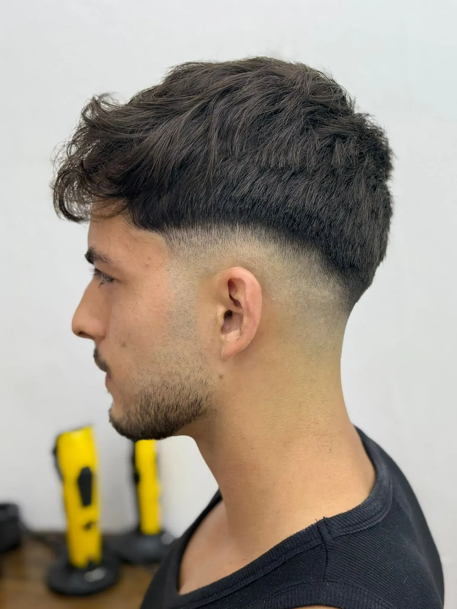 Hombre con cabello oscuro y corte de pelo descolorido, mirando hacia la izquierda.