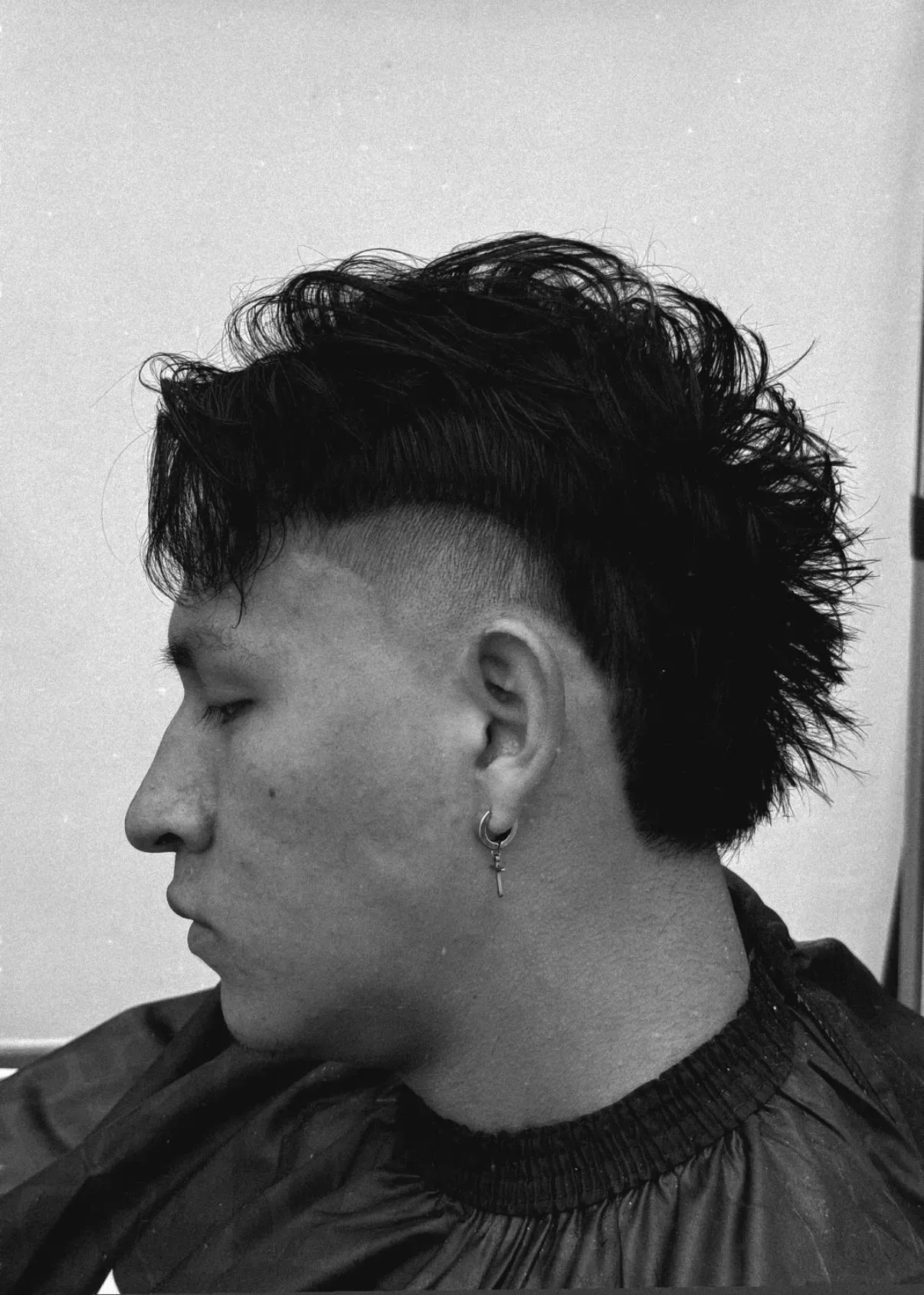 Hombre con un peinado mohawk descolorido, vista de perfil lateral, vistiendo una camisa oscura.