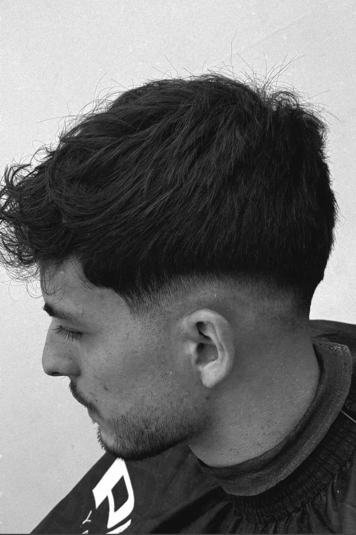 Hombre con cabello oscuro y corte de pelo descolorido, mirando hacia la izquierda.