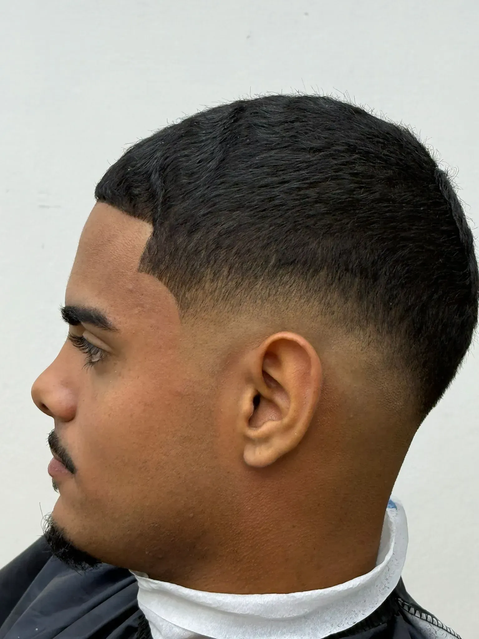 Hombre con un corte de pelo degradado de piel oscura, degradado desde la piel hasta el cabello oscuro en la parte superior.