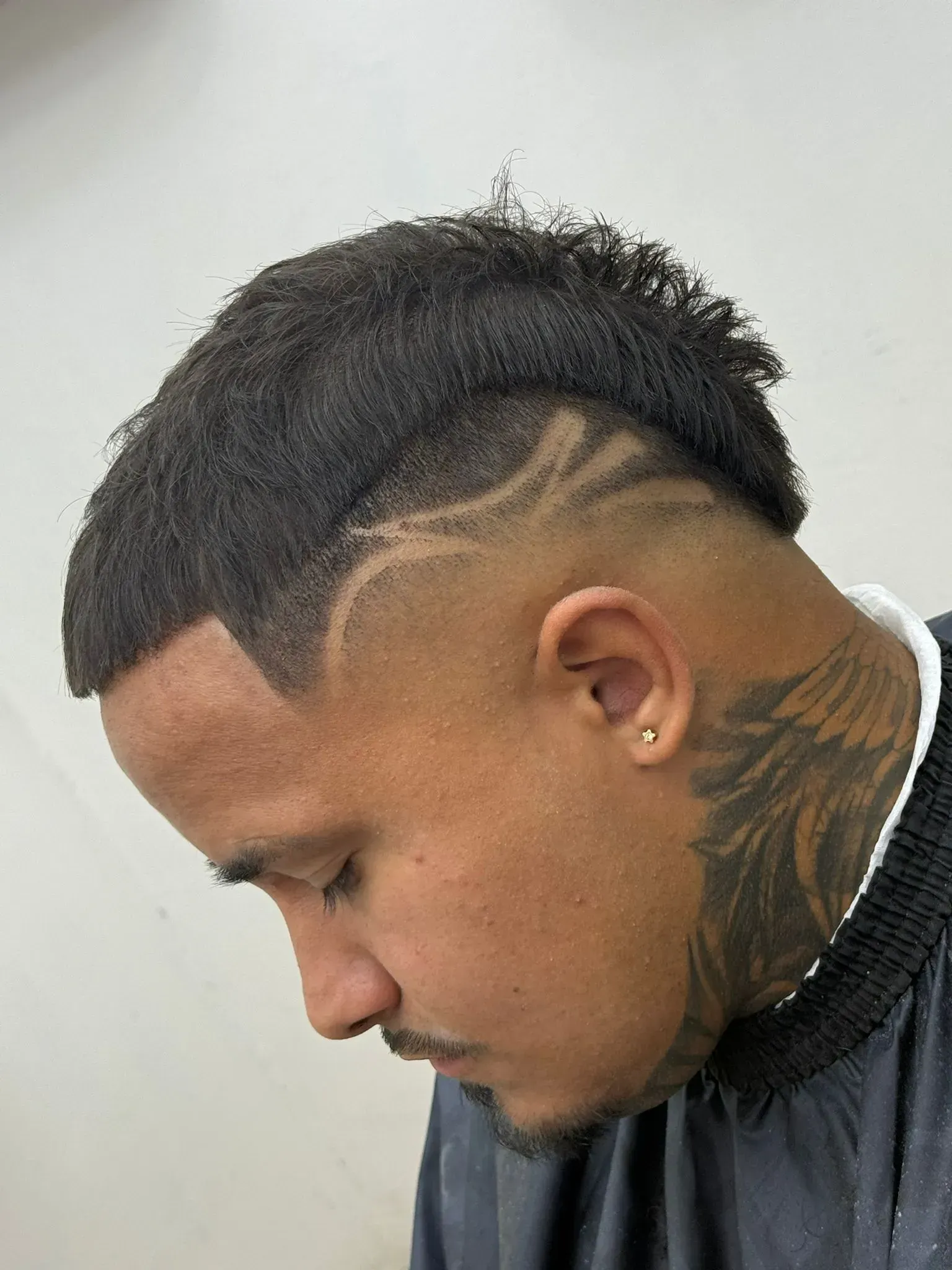 Hombre de piel oscura, corte de pelo bajo y tatuaje en el cuello, mirando hacia la izquierda.