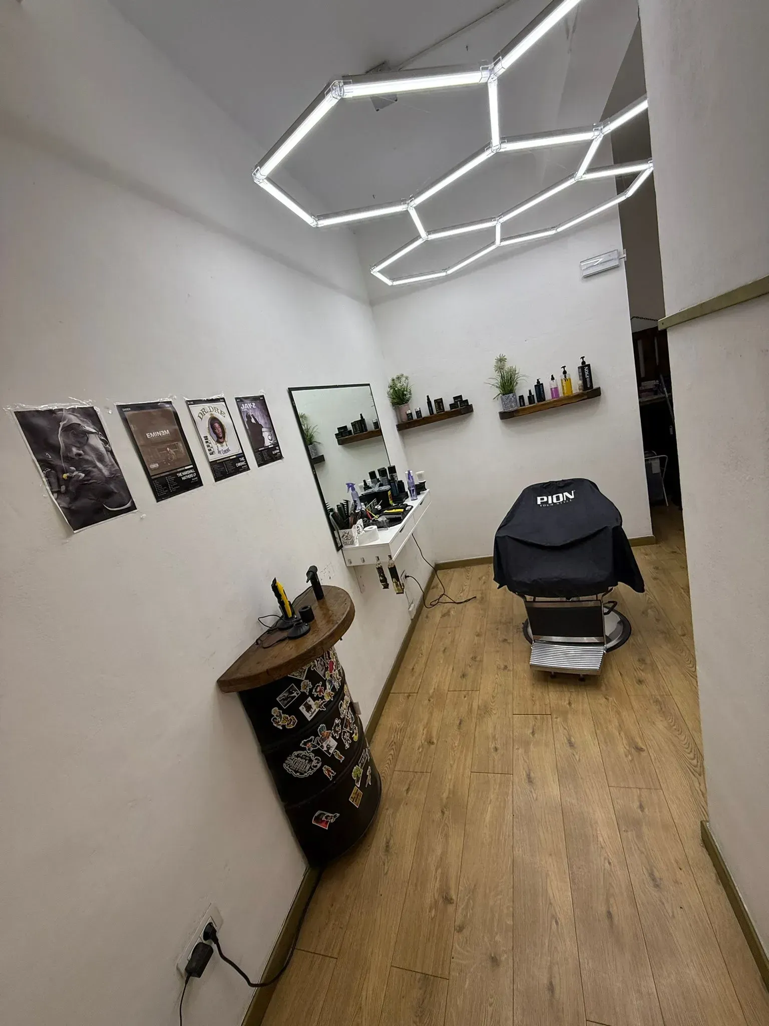 Interior de barbería con luces hexagonales, silla de barbero, espejo y estantes con productos.