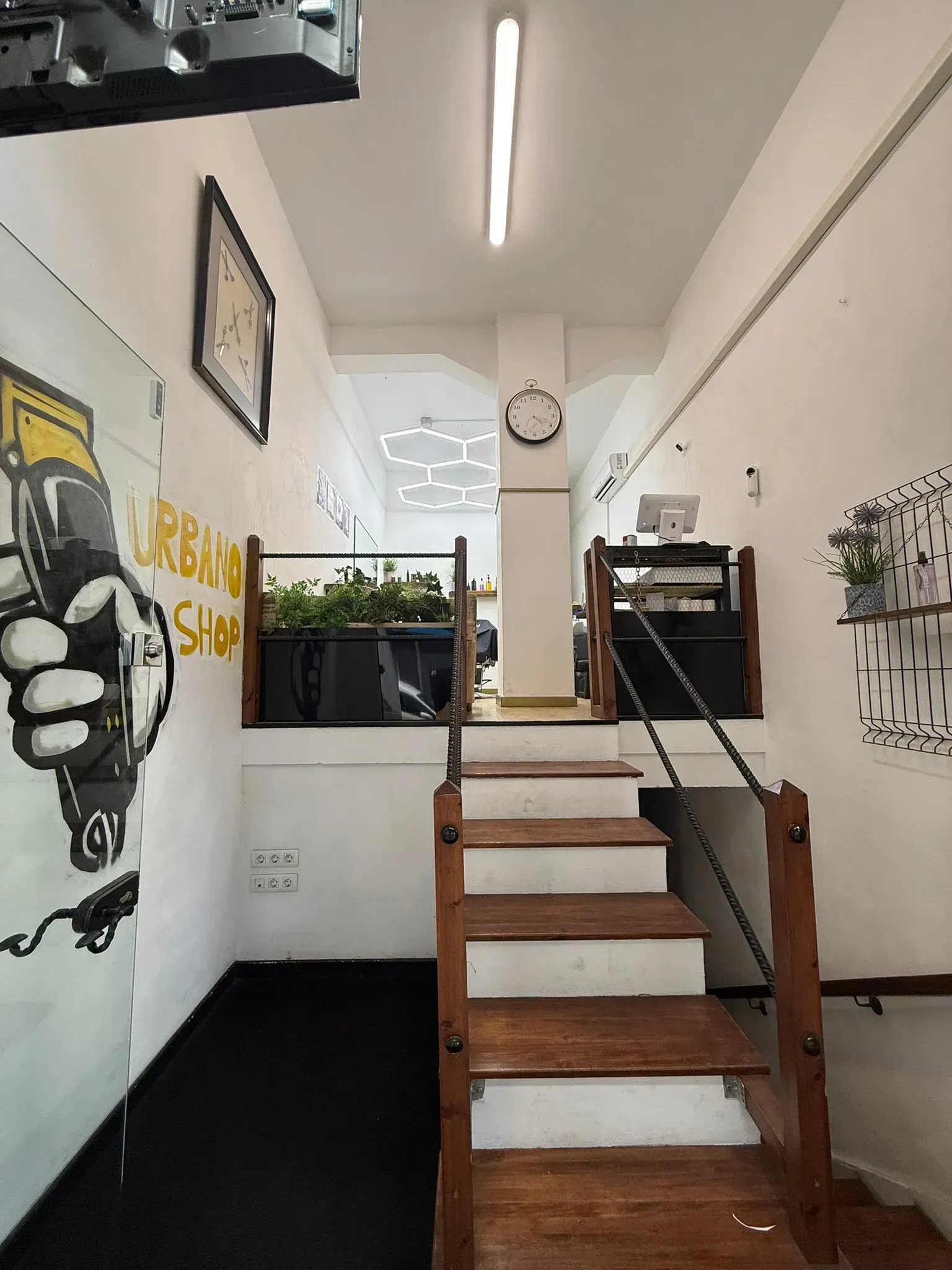 Interior de una barbería con escaleras que conducen a un nivel superior; arte de pared en blanco y negro de una máquina cortadora.