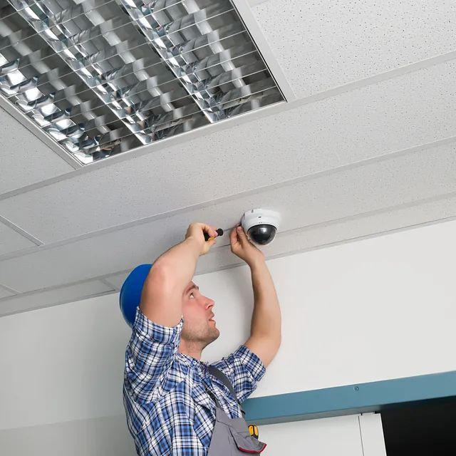 Un hombre está instalando una cámara de seguridad en el techo.