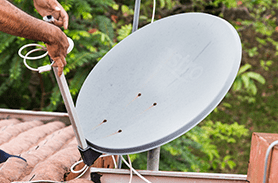 Un hombre está instalando una antena parabólica en un tejado.