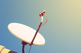 Una antena parabólica está colocada sobre un tejado contra un cielo azul.