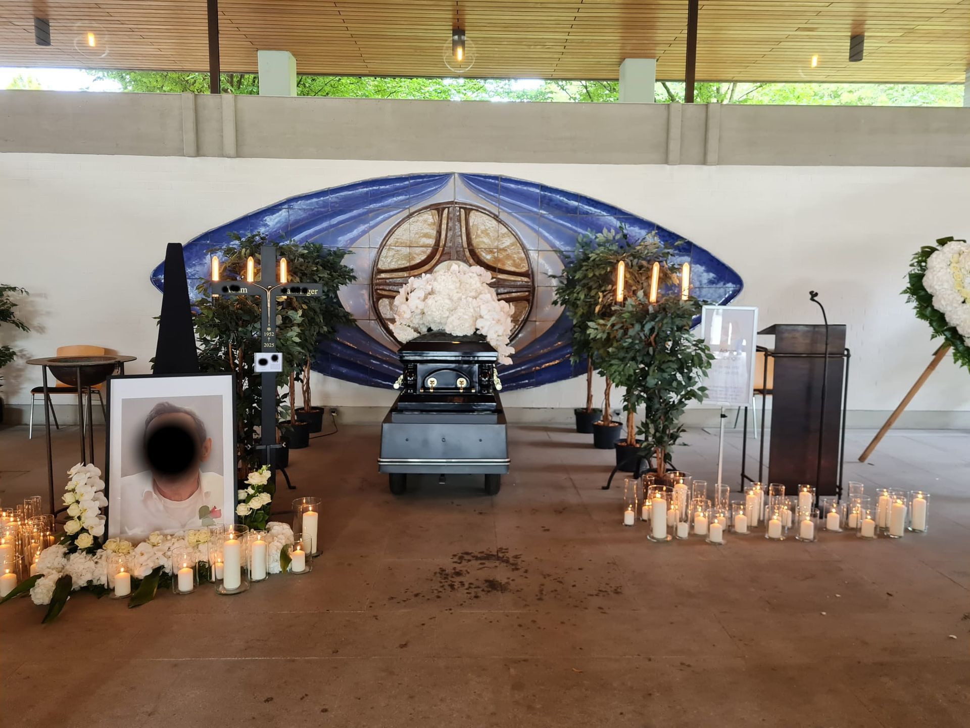 Sarg unter Blumenbaldachin, umgeben von Kerzen und Blumenschmuck.