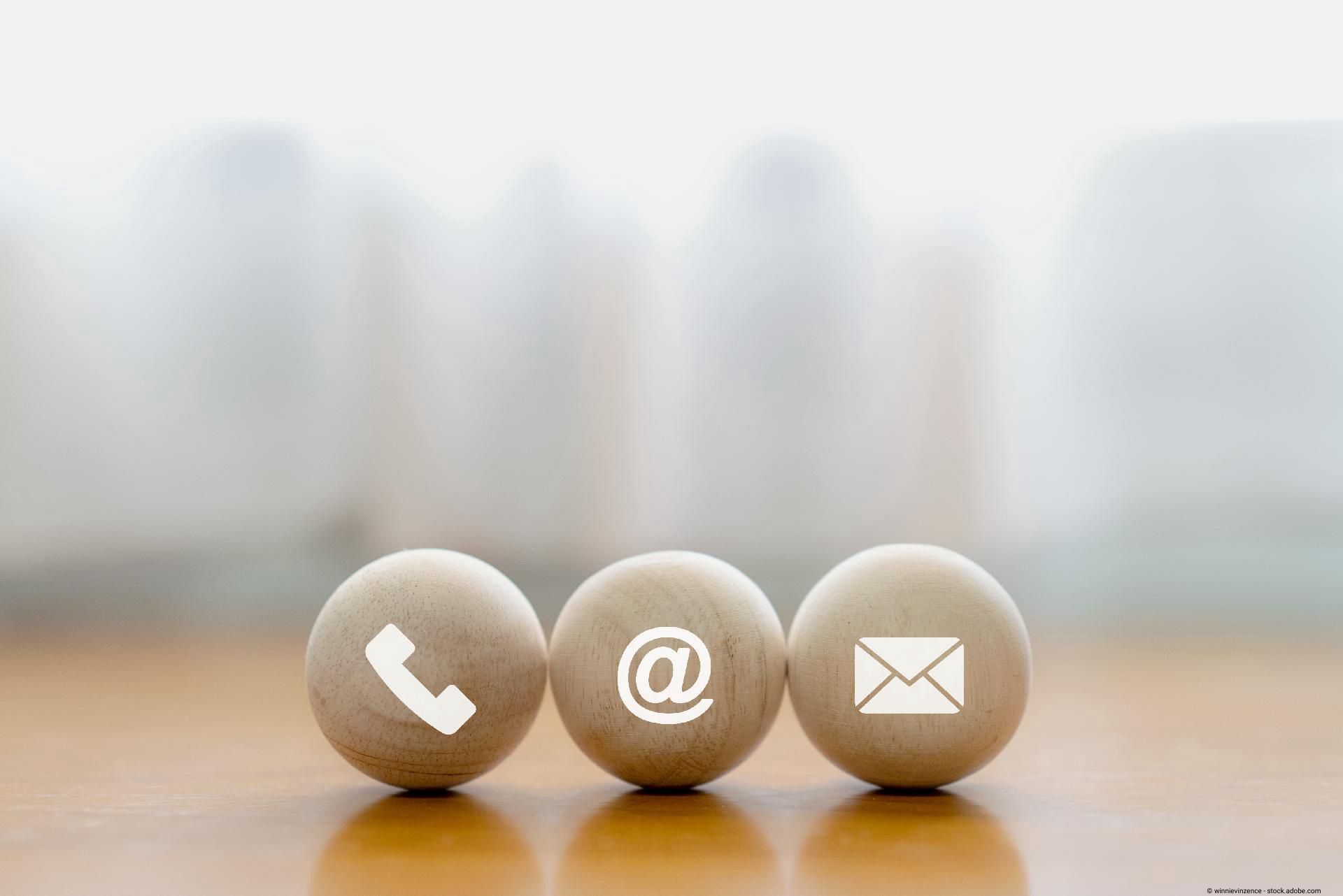 Drei Kugeln mit Symbolen für Telefon, E-Mail und Kontakt vor unscharfem Hintergrund.