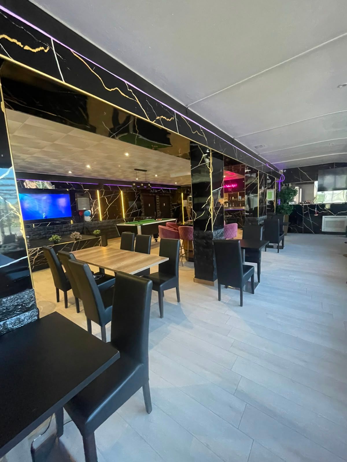 Salle de restaurant moderne la nuit, avec chaises noires, tables en bois et murs en miroir.