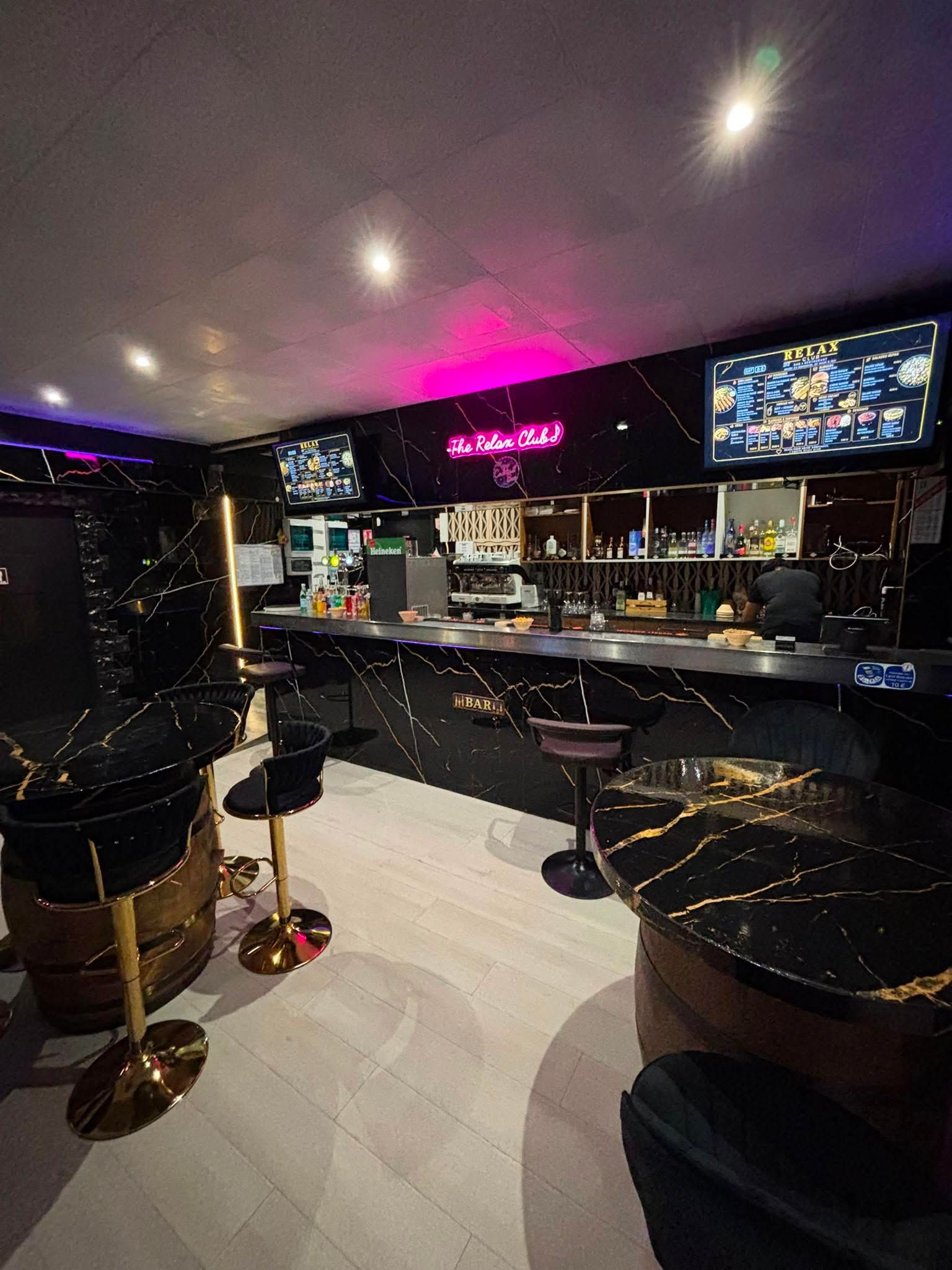 Bar moderne avec tabourets noirs, enseigne rose fluo et écrans de télévision lumineux dans un salon sombre