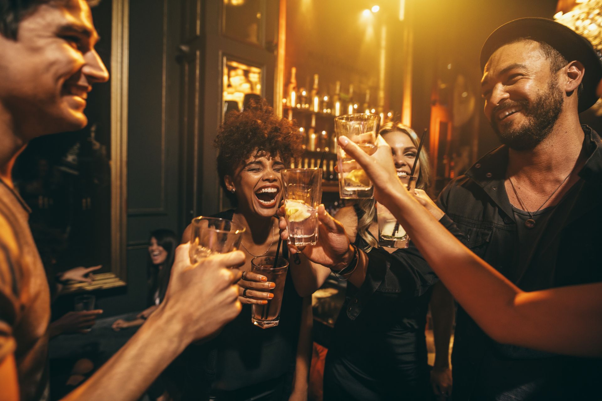 Des amis trinquent dans un bar à l'éclairage chaleureux, souriant et riant ensemble.