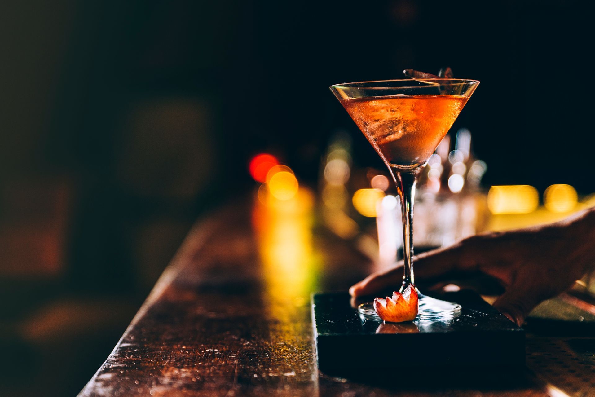 Un cocktail dans un verre à martini sur un comptoir de bar faiblement éclairé, avec des lumières floues en arrière-plan.
