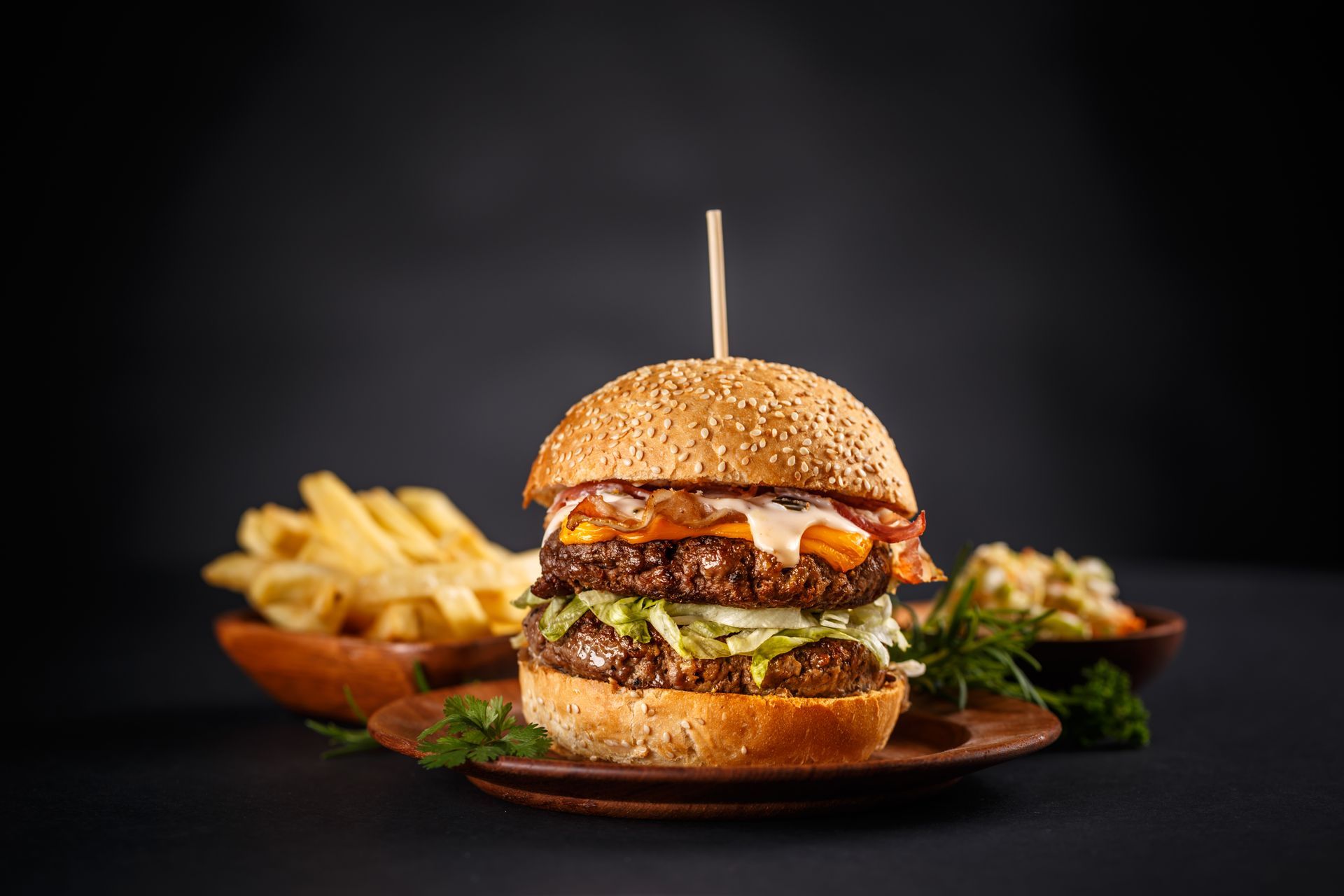 Cheeseburger juteux avec frites sur fond sombre, servi sur une planche en bois avec une brochette.