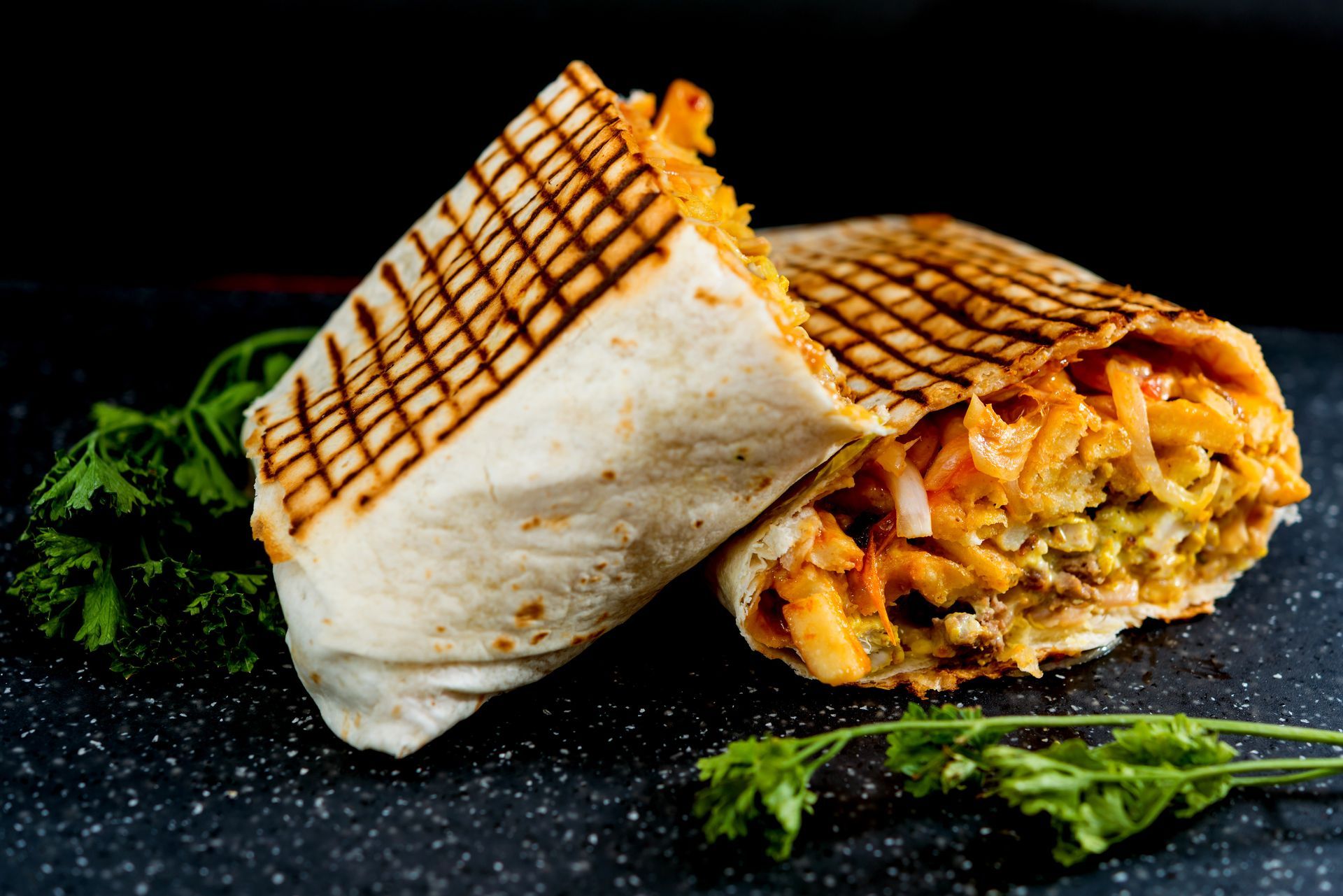 Wrap grillé coupé en deux, révélant une garniture au fromage sur une assiette foncée, garnie de persil.