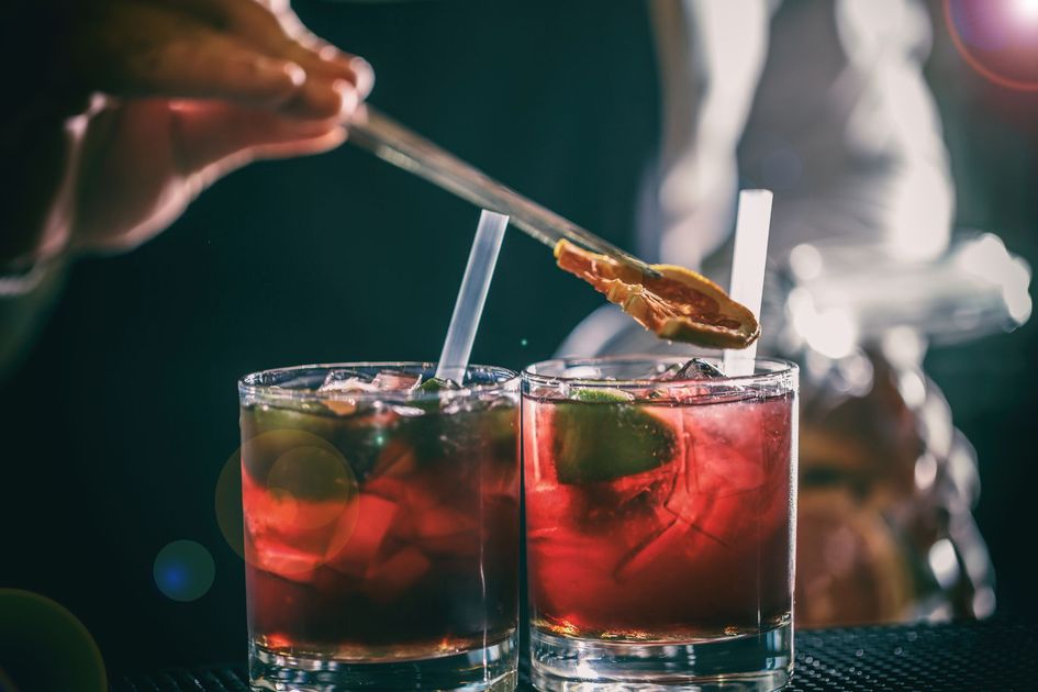 Deux cocktails rouges servis dans des verres avec des pailles, décorés à la main à l'aide d'une cuillère dans un bar à l'éclairage tamisé.