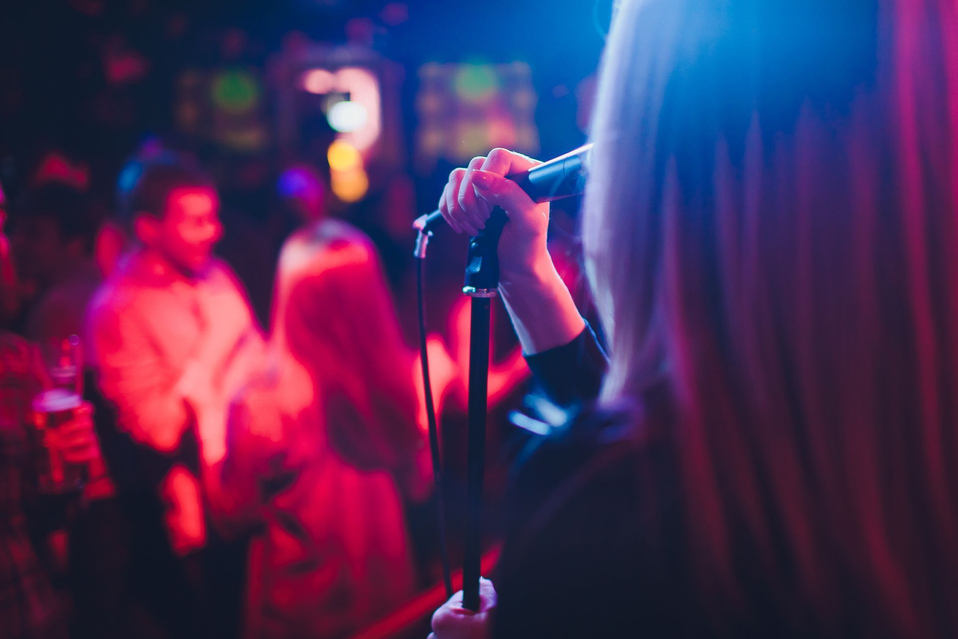 Une chanteuse tenant un micro sur une scène colorée et floue, avec le public en arrière-plan.