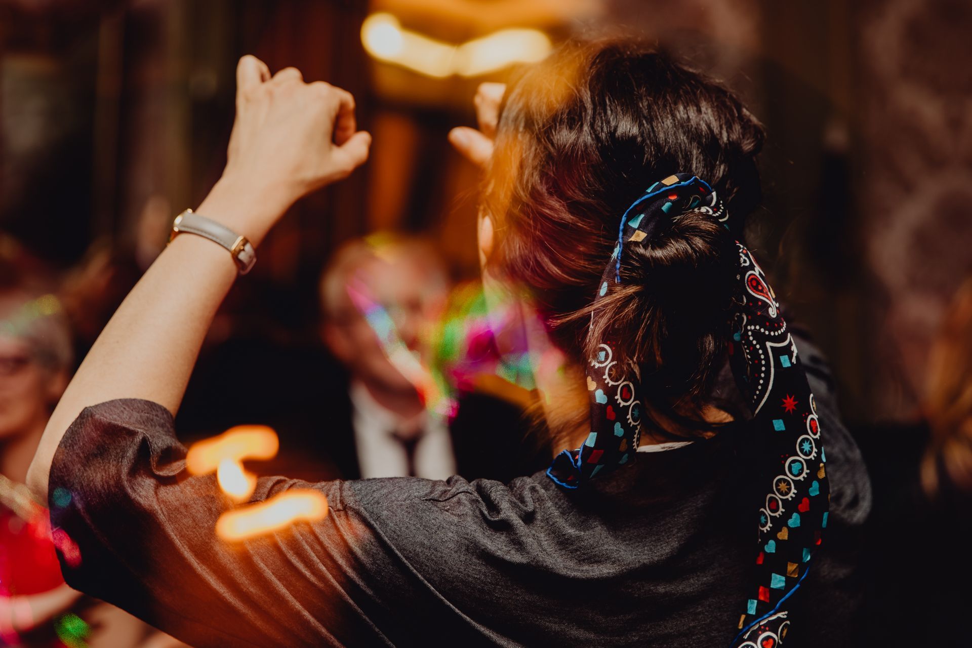 Femme dansant les bras levés lors d'une fête animée, vêtue d'une robe sombre à broderies colorées et coiffée d'une tresse.