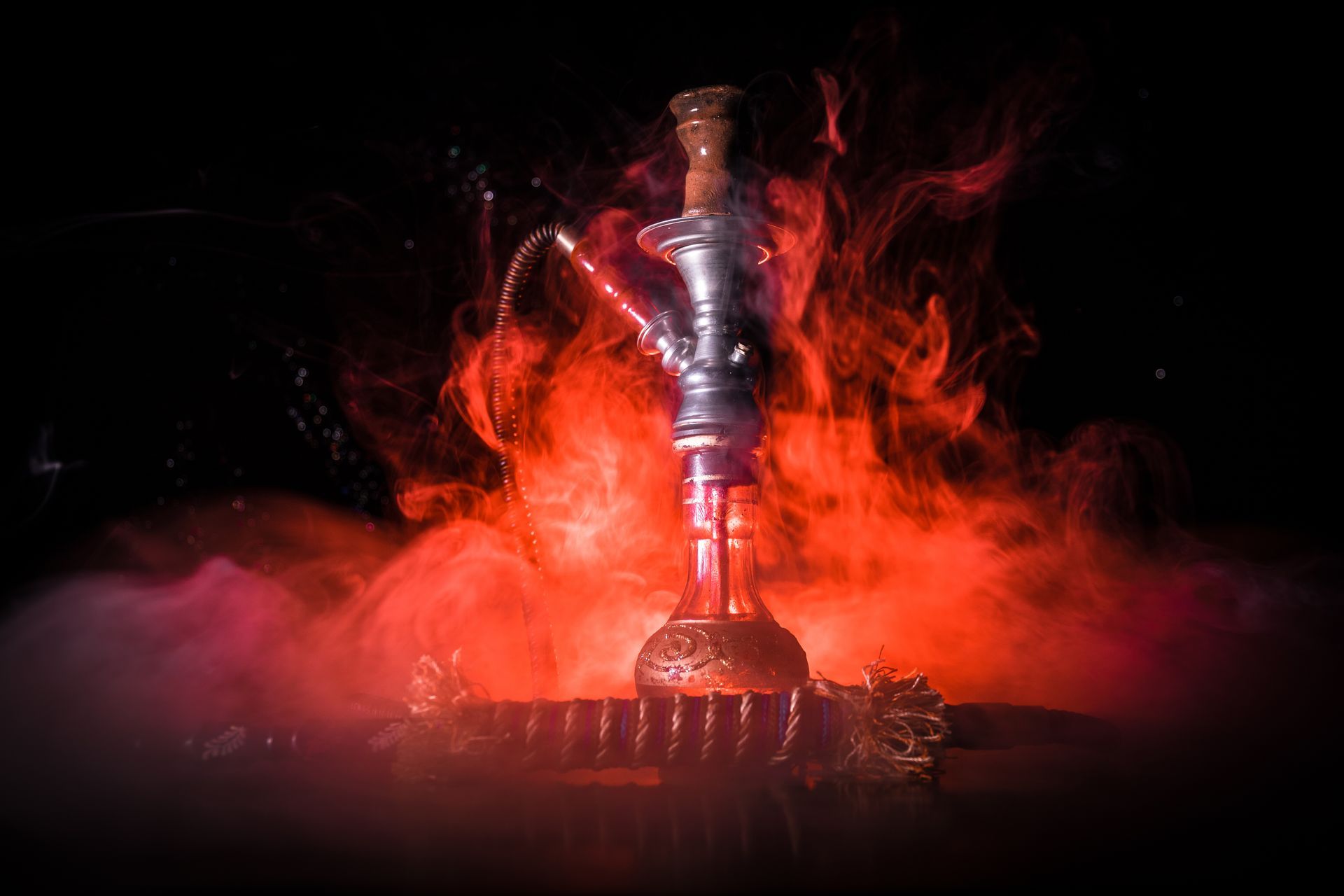 Une e-chicha argentée entourée d'une fumée rouge et de flammes sur un fond sombre.