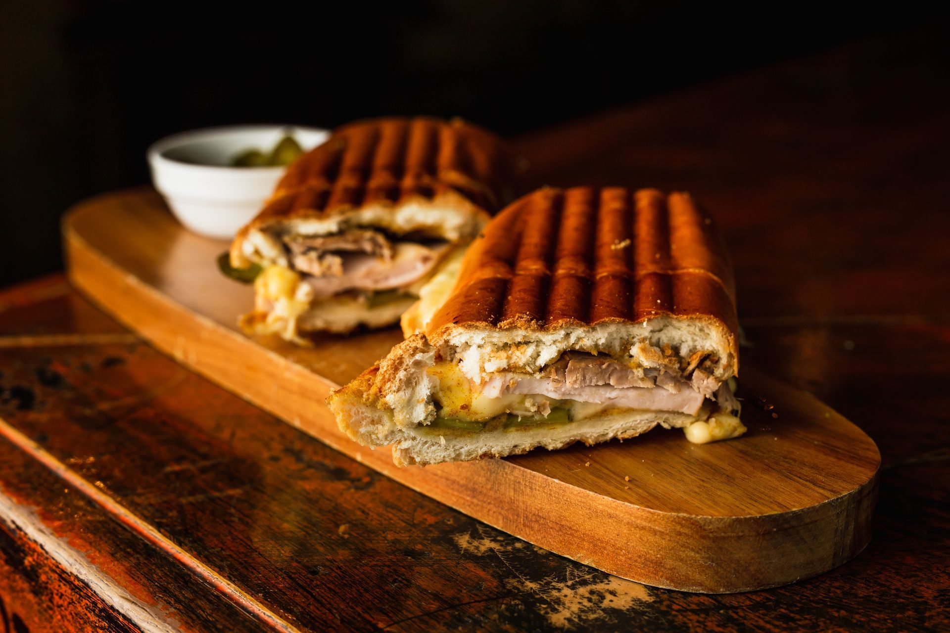 Moitiés de paninis sur une planche en bois avec un petit bol de sauce.