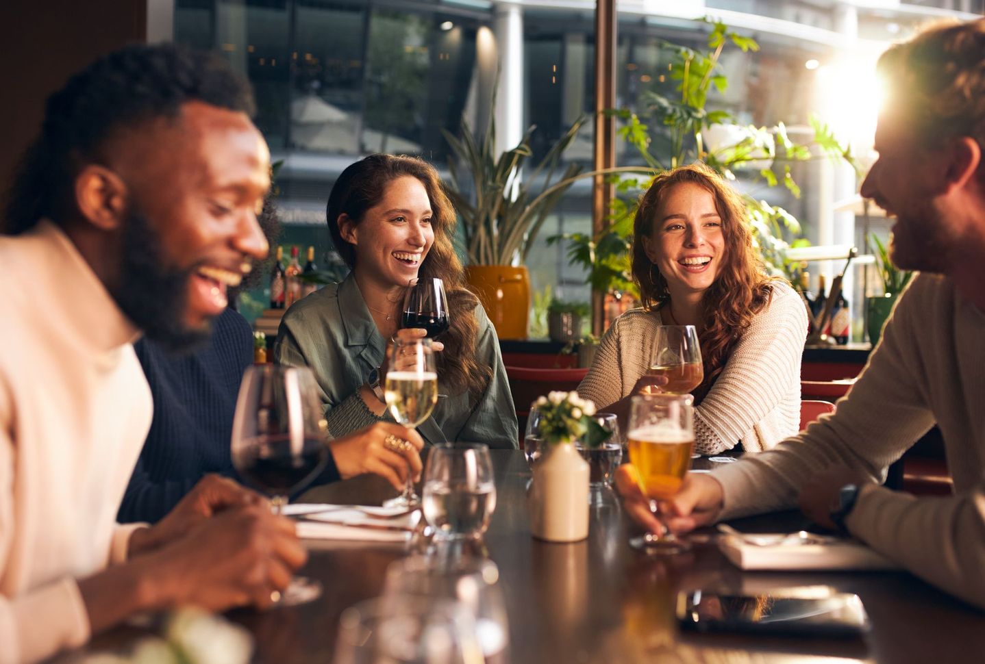 Des amis discutent et rient autour d'un verre à une table de restaurant à l'éclairage chaleureux