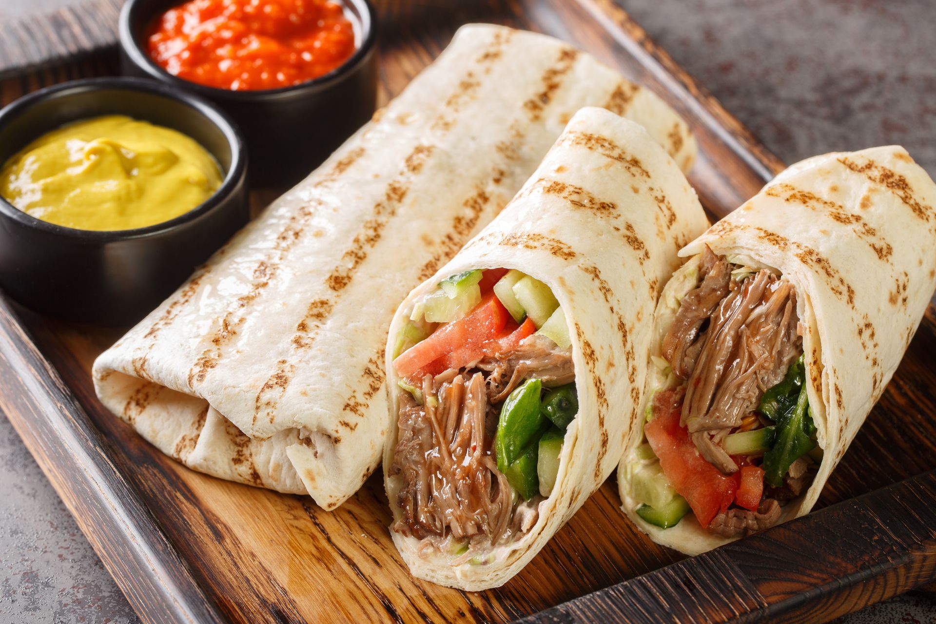 Sandwichs roulés grillés au bœuf et aux légumes, servis sur une planche en bois avec des sauces à tremper à part.