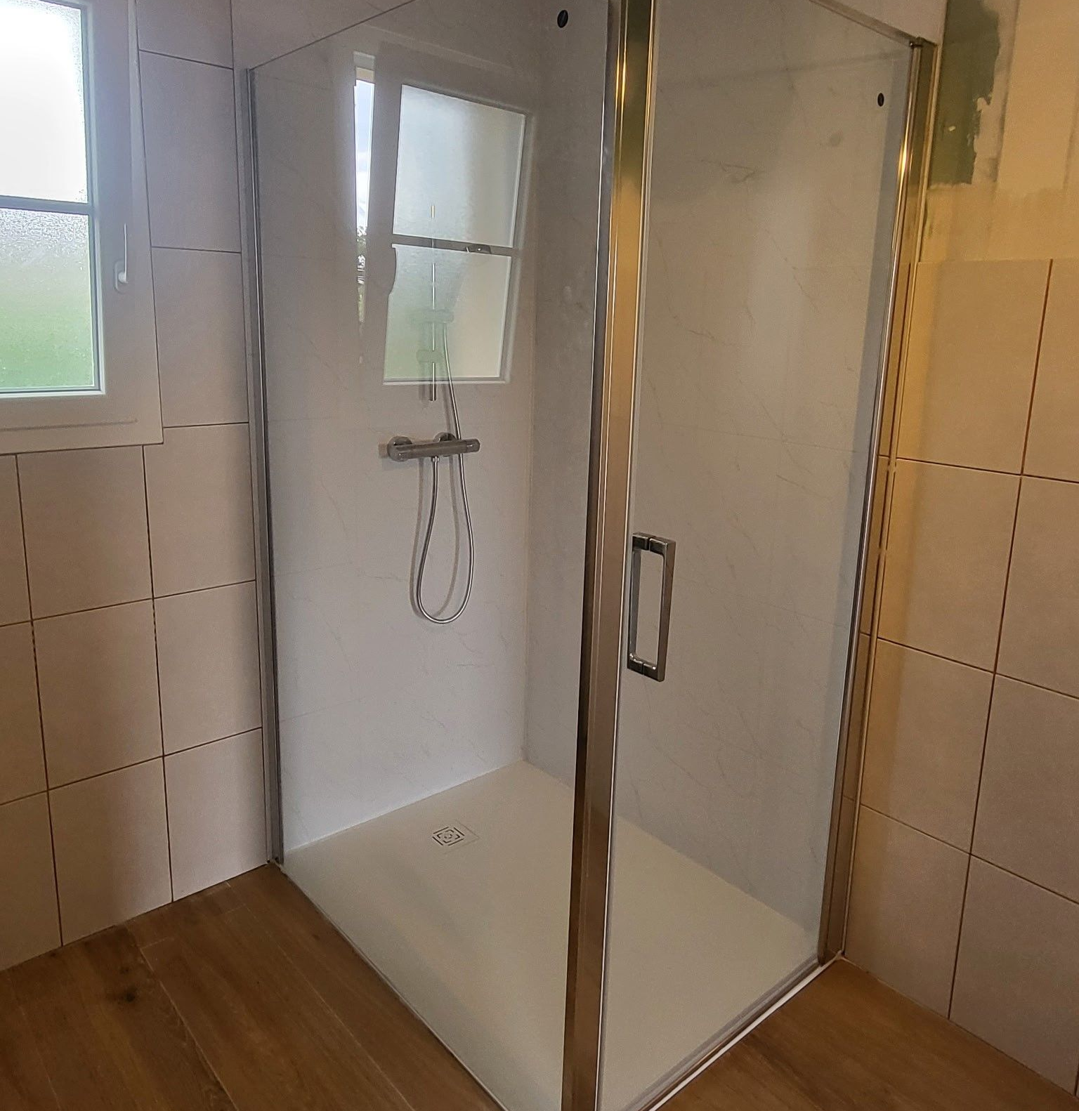 Cabine de douche avec portes en verre, murs, robinetterie et fenêtre.