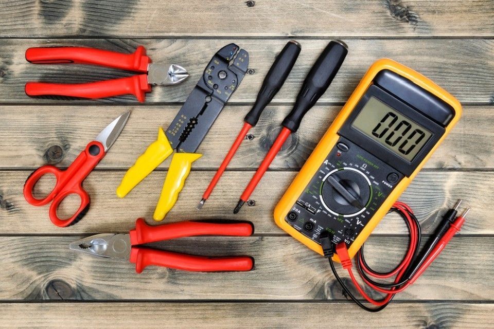 Joukko työkaluja ja digitaalinen yleismittari puupöydällä.