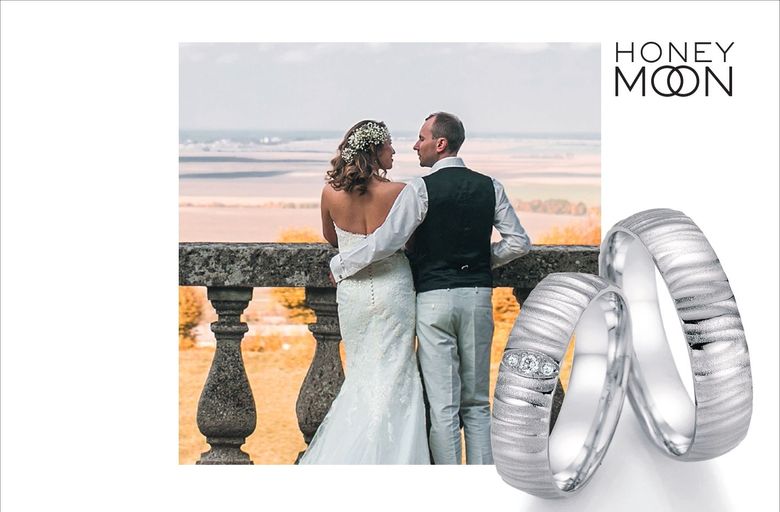 Brautpaar an einem Steingeländer und silberfarbene Eheringe von Honey Moon