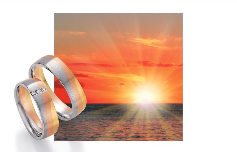 Sonnenuntergang über dem Meer und zwei mehrfarbige Trauringe