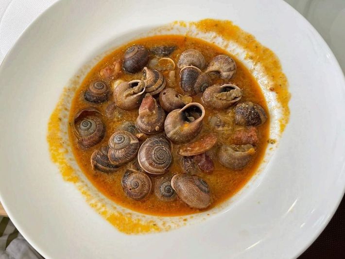 Plato de caracoles cocidos en salsa de naranja sobre un plato blanco.