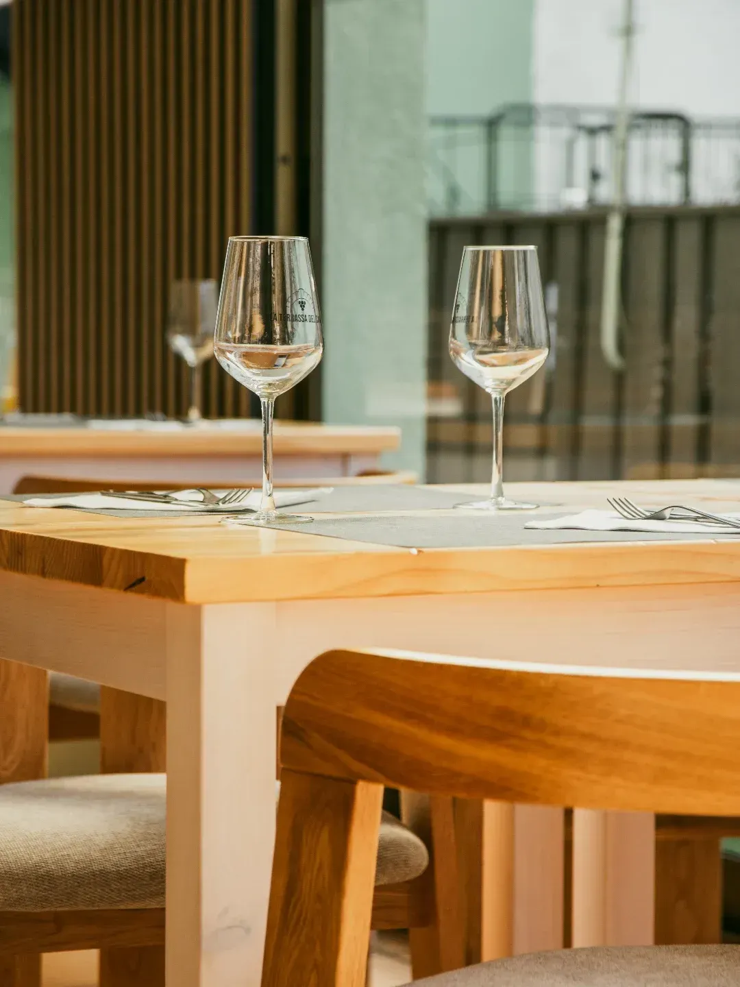Dos copas de vino sobre una mesa de madera en un restaurante moderno y luminoso.