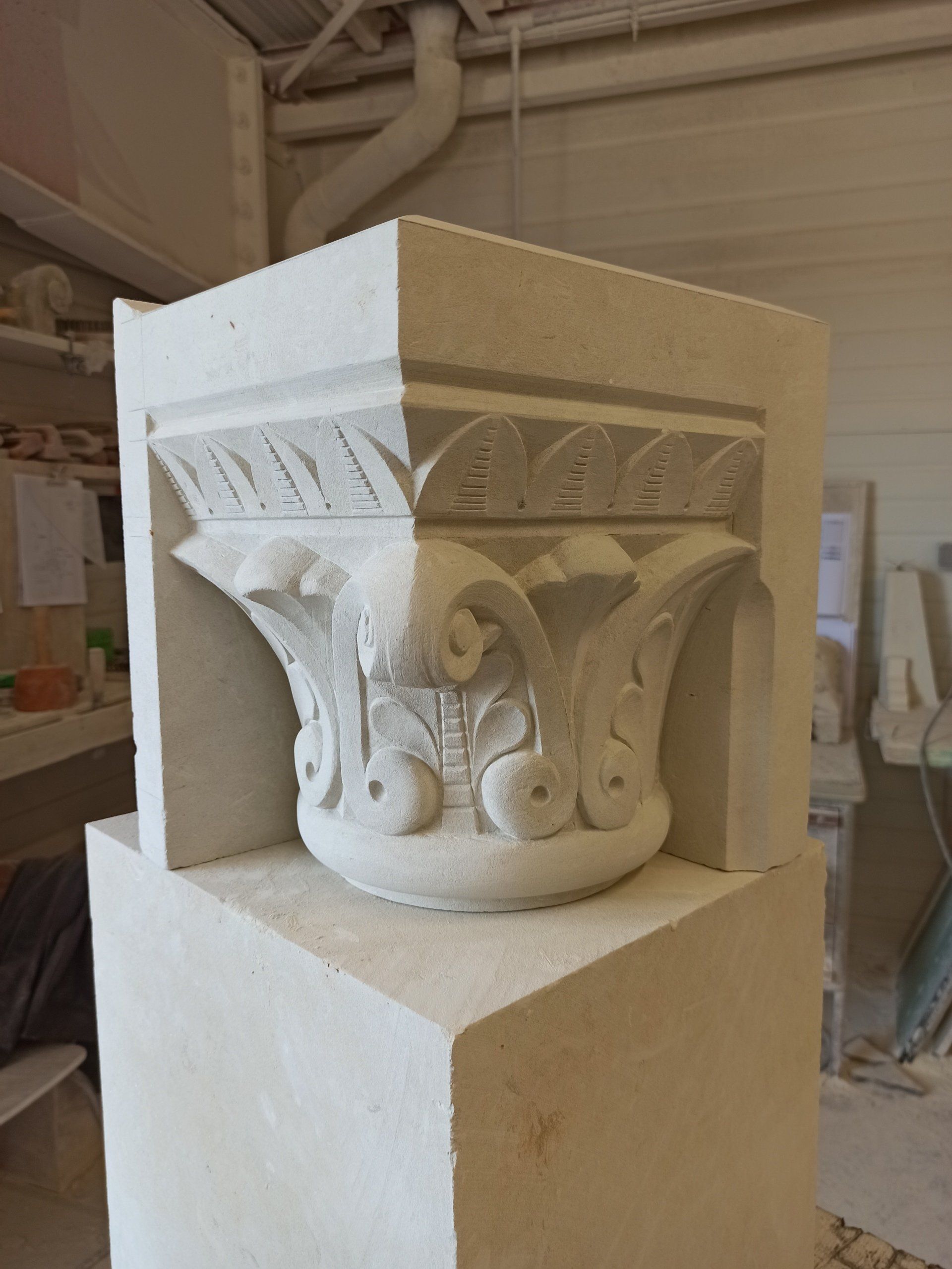 Chapiteau en pierre blanche sculptée, orné de feuilles et de volutes, exposé sur un socle dans un atelier