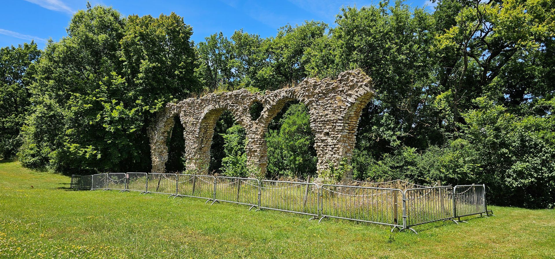 Arche de pierre en ruine au milieu d’un champ verdoyant, entourée d’arbres sous un ciel bleu éclatant