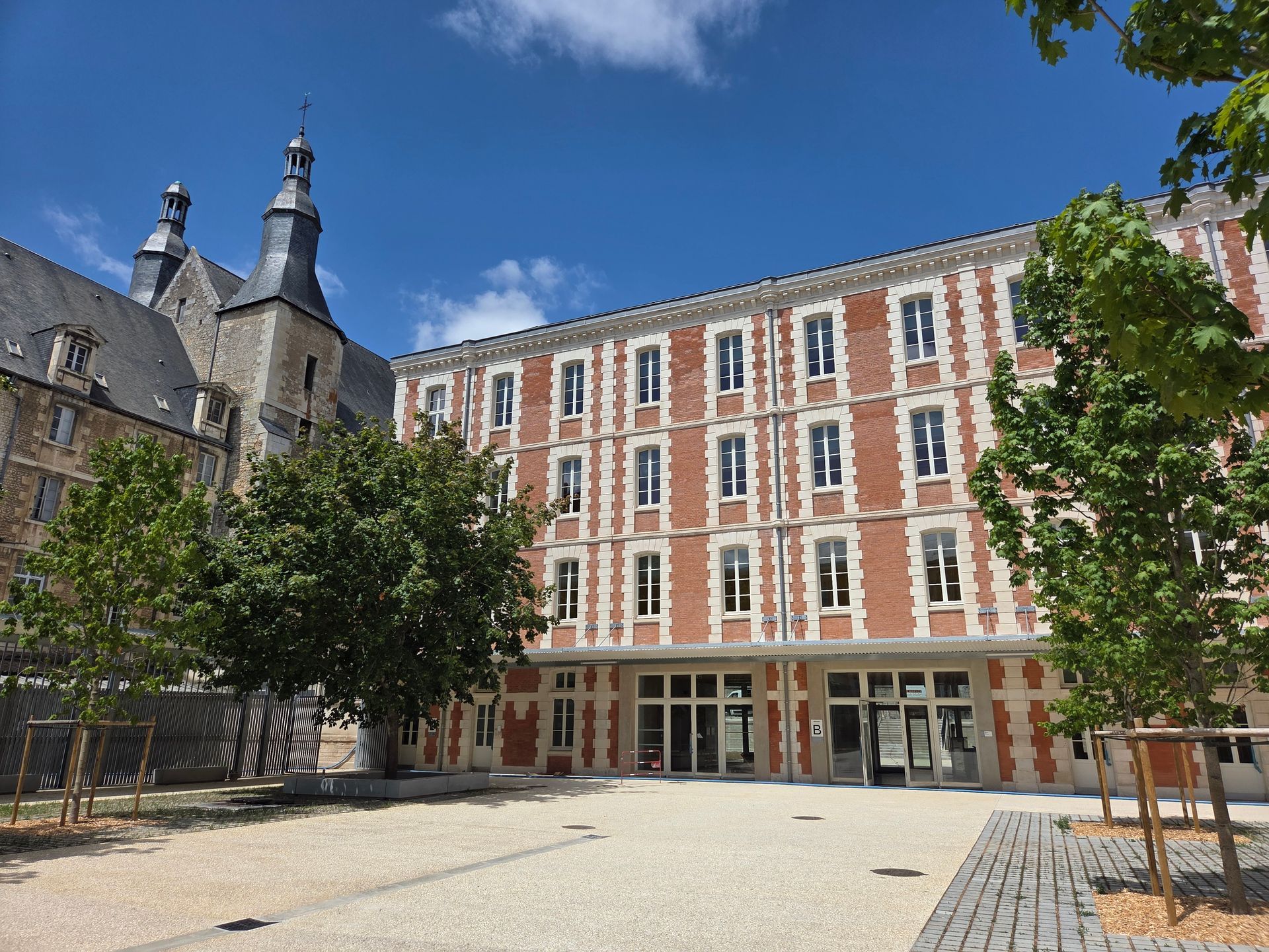 Cour intérieure d’un bâtiment historique en briques, avec un clocher sous un ciel bleu