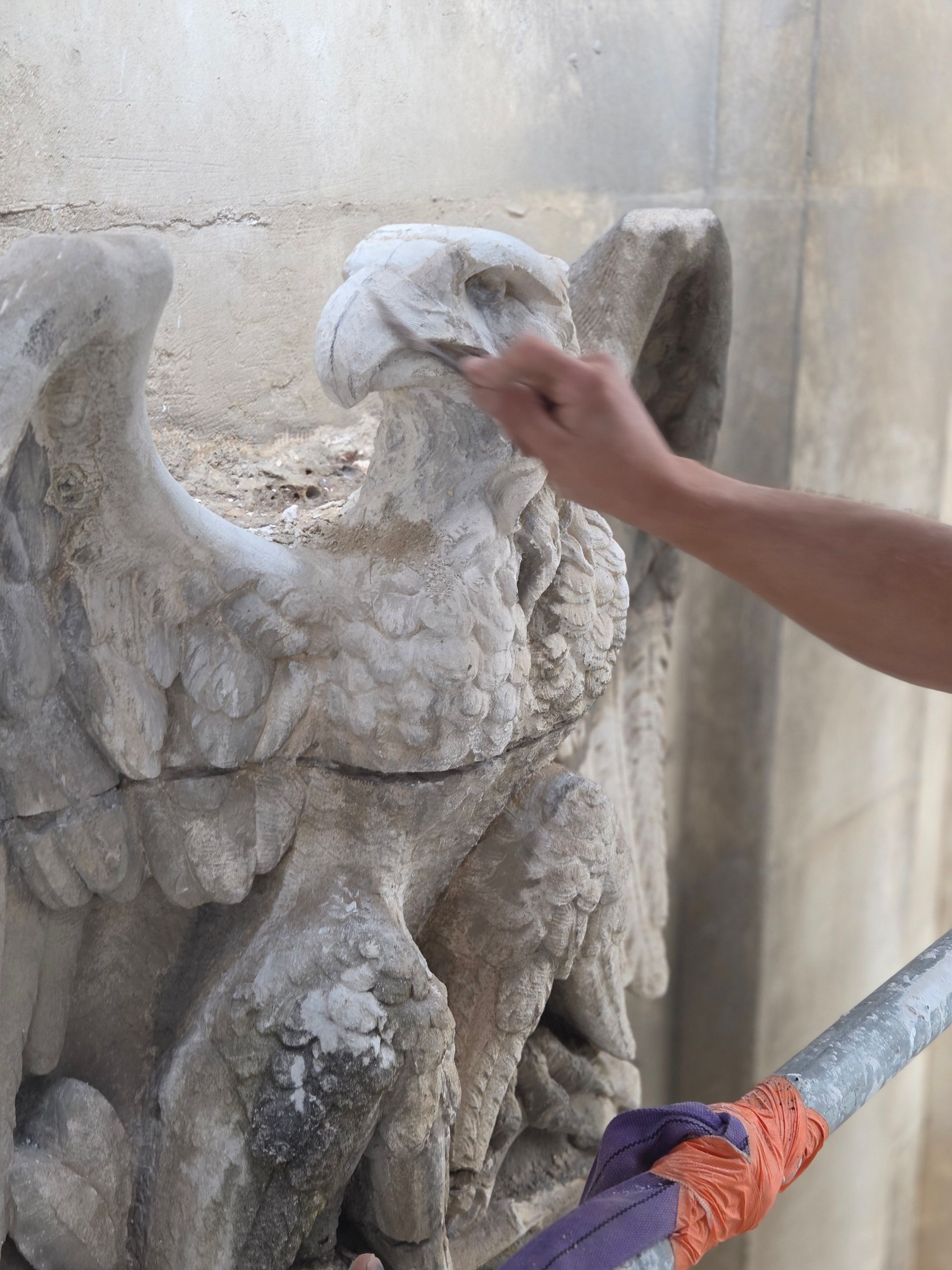 Nettoyage manuel d’une sculpture d’aigle en pierre patinée avec un chiffon, en extérieur