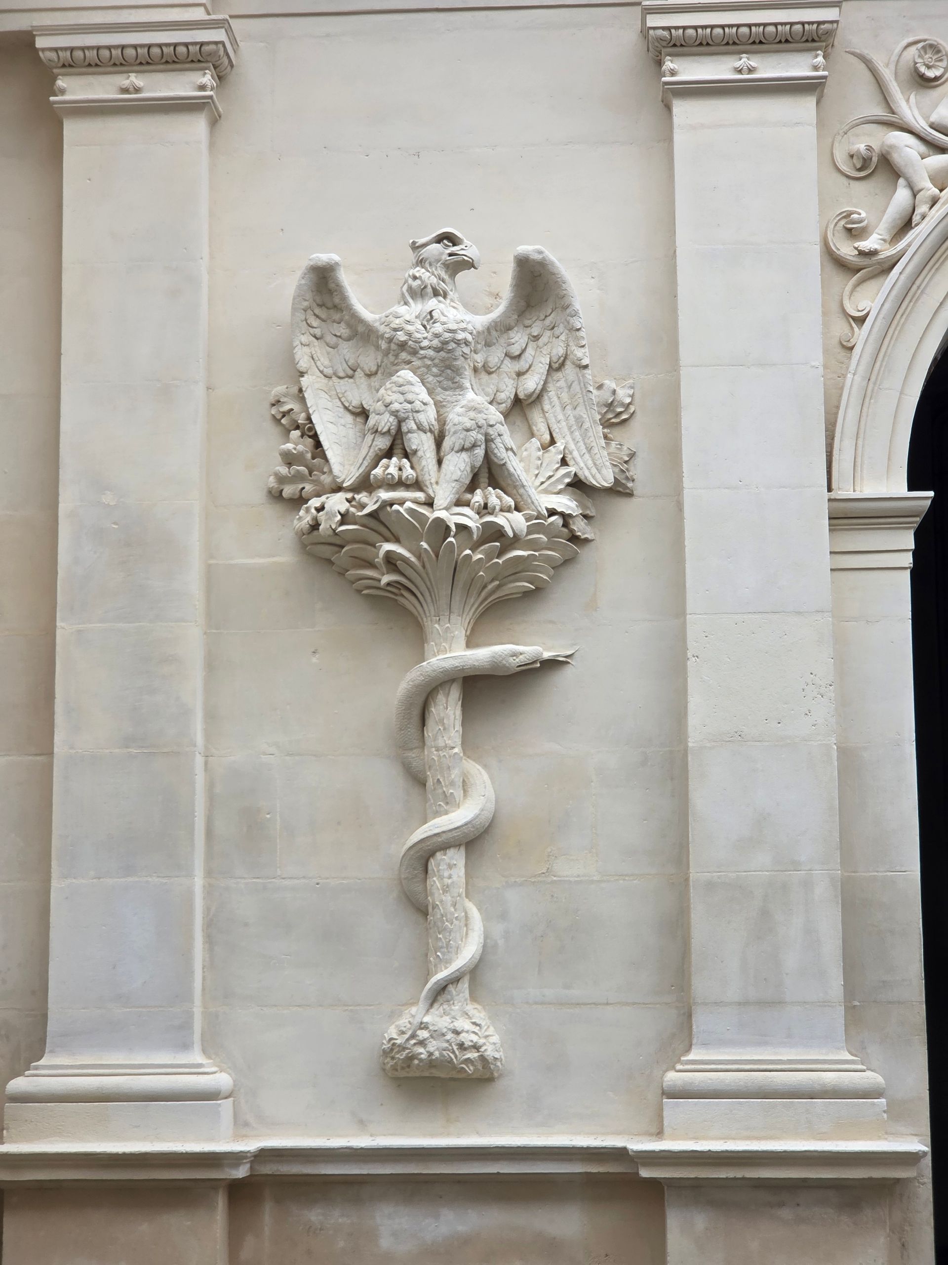Bas-relief en pierre représentant un aigle et un serpent sur le mur d’un bâtiment, entre des colonnes