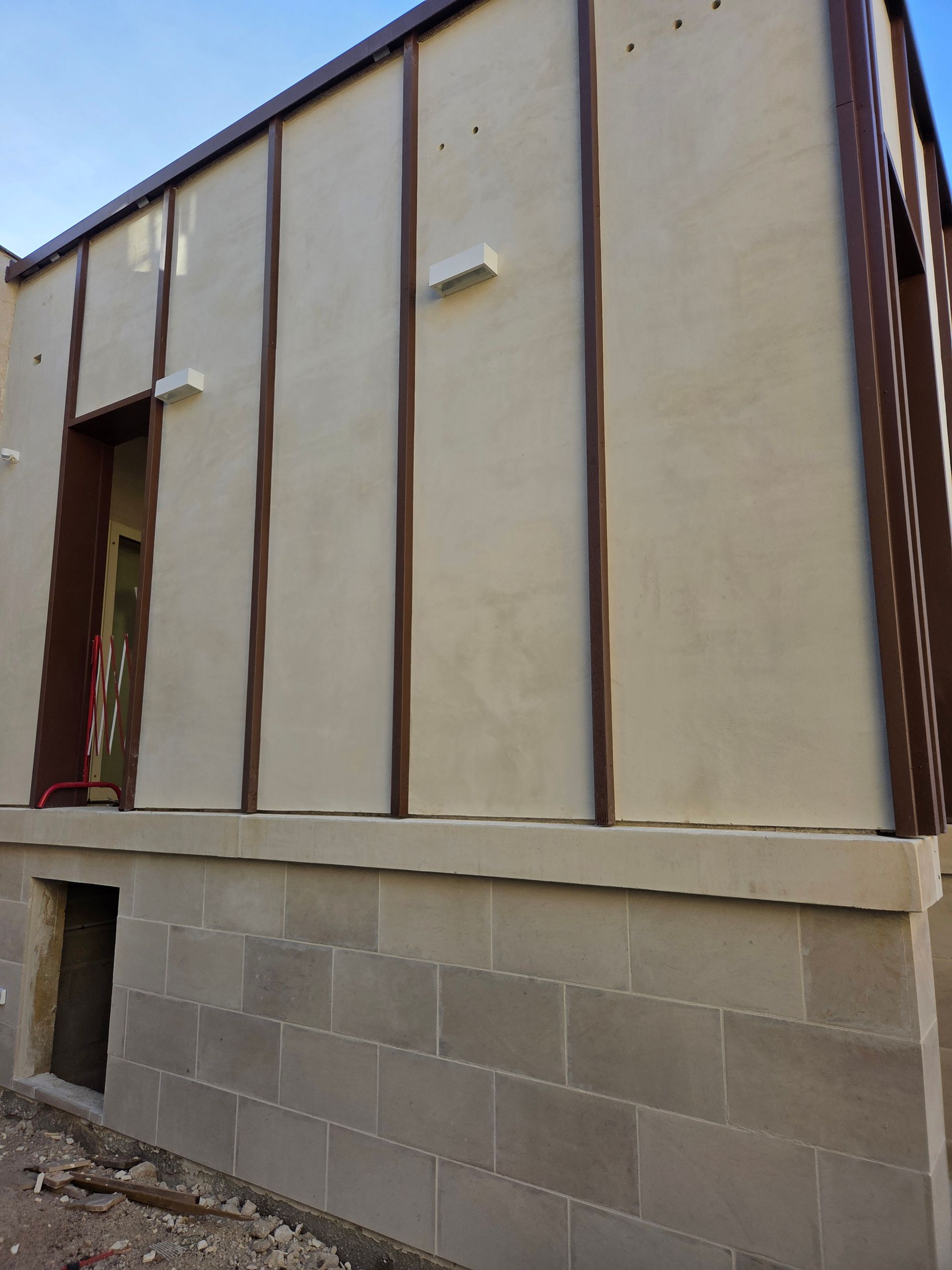 Mur extérieur avec un bardage crème et des garnitures brunes au-dessus d’un soubassement en parpaings