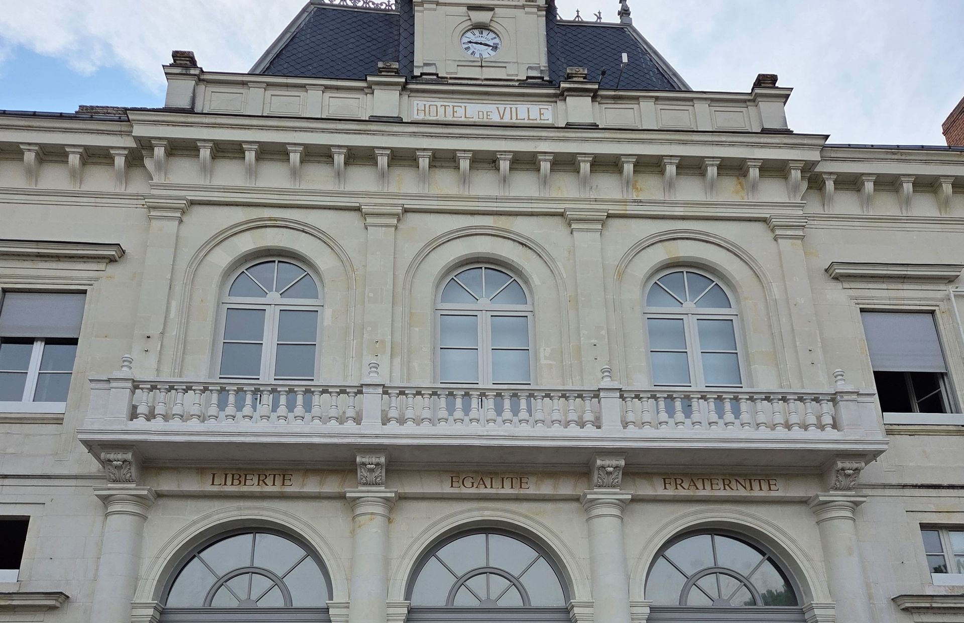 Façade d’un bâtiment historique orné, avec des fenêtres cintrées et un toit en ardoise