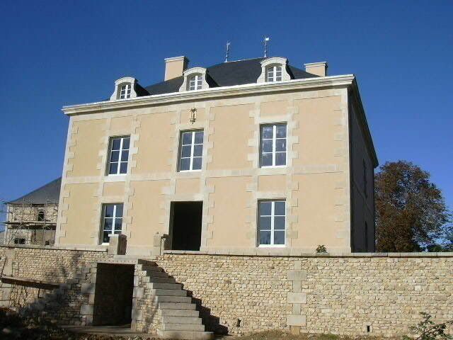 Bâtiment en pierre à la façade beige et aux lucarnes, vu d’en bas sous un ciel bleu.