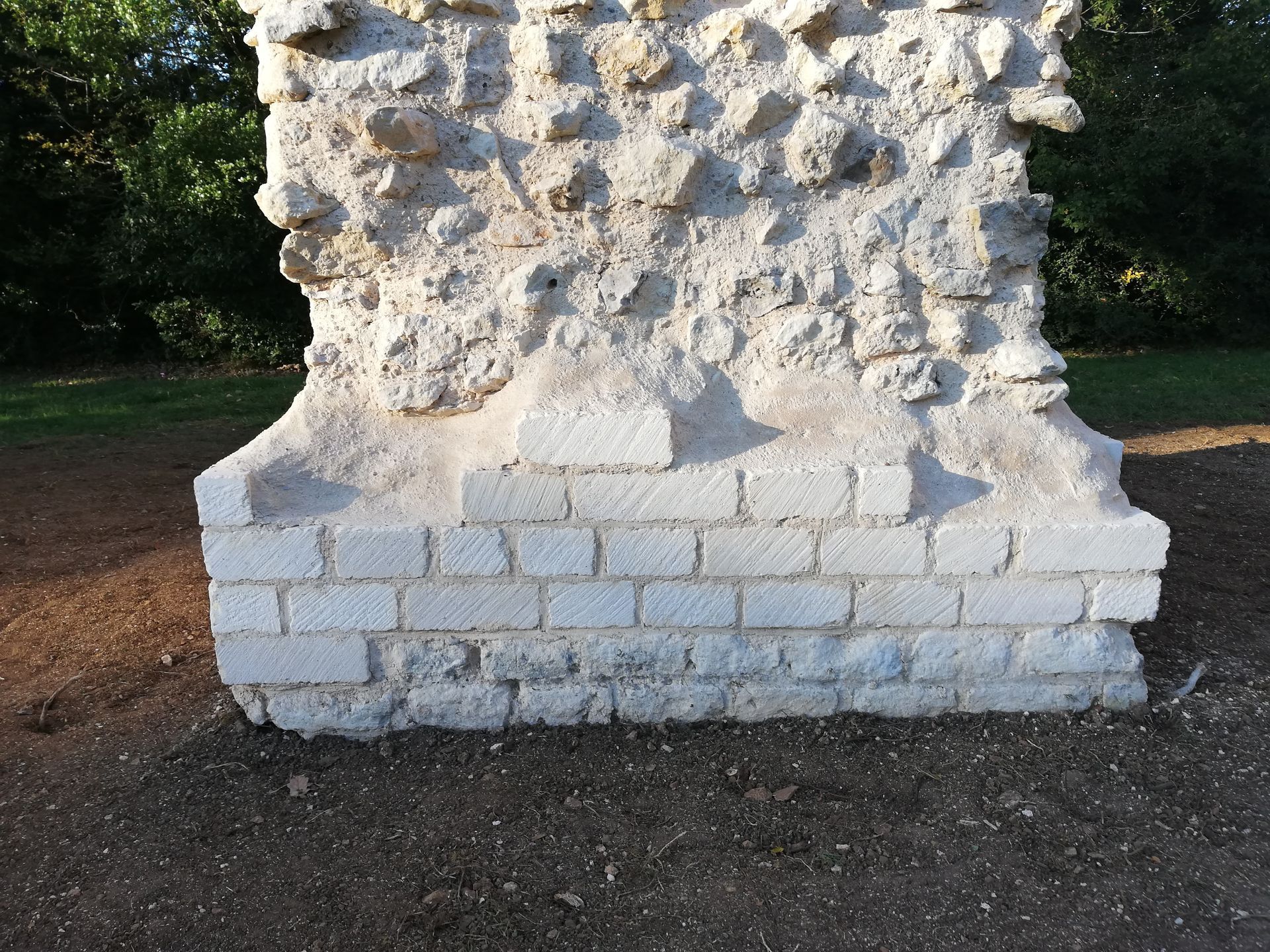 Socle de sculpture en pierre sur un sentier de terre dans un espace boisé en plein air