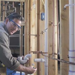 Un lampista amb ulleres de seguretat treballa en canonades en una habitació parcialment construïda.
