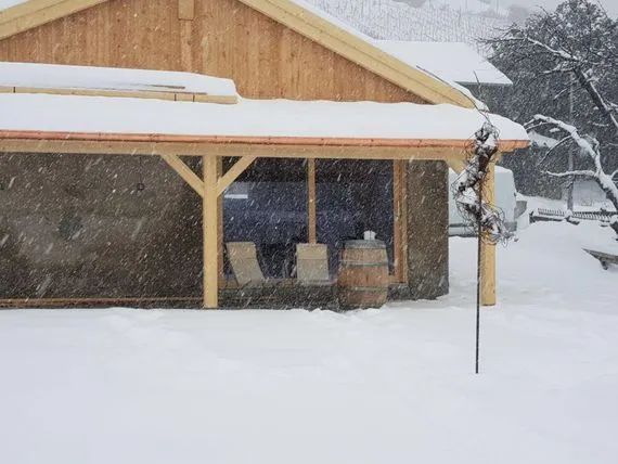 Une maison enneigée avec un tonneau devant