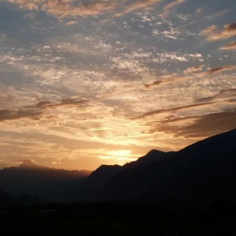 Un coucher de soleil sur une chaîne de montagnes avec un ciel nuageux