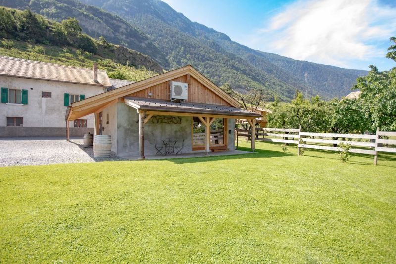 Une maison avec une clôture devant et des montagnes en arrière-plan.