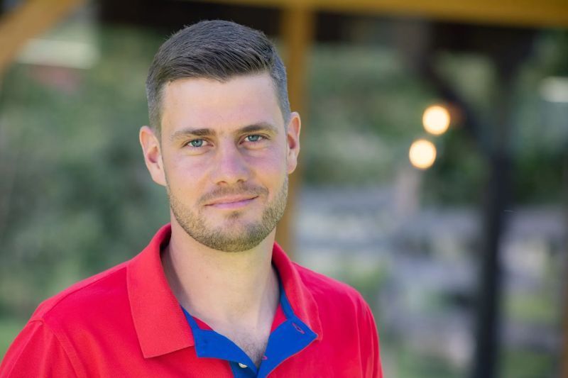 Un homme en chemise rouge et chemise bleue se tient devant un belvédère.