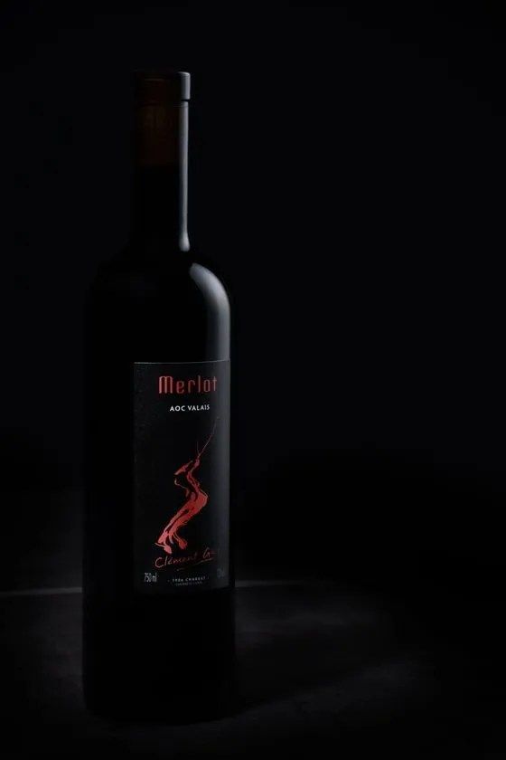 Une bouteille de vin merlot est posée sur une table sur un fond noir.