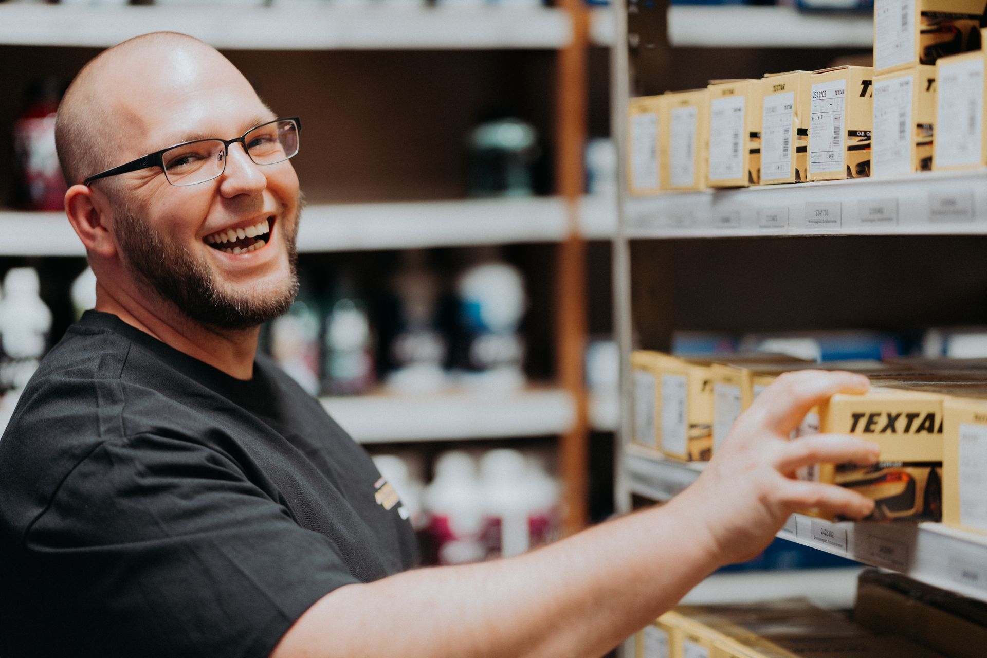 Ein Mann lächelt, während er in einem Lagerhaus eine Kiste hält.